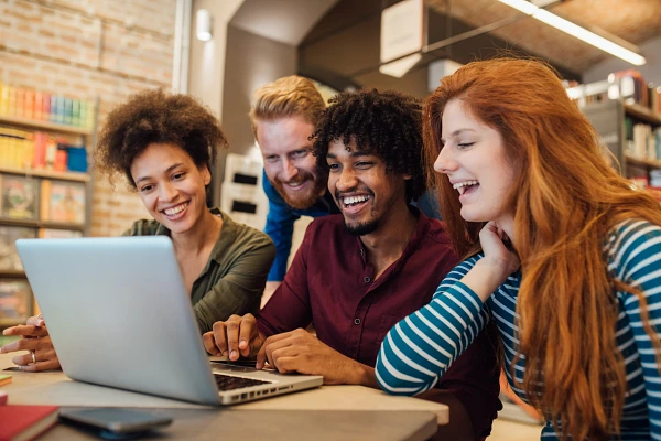 Four students gathered at at table, looking at a laptop together